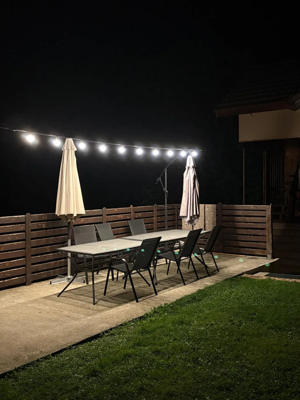 Terasa cu masă, umbrele și ghirlande luminoase seara, la Edant House